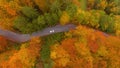 AERIAL: Cars cruise along empty road leading through the forest changing leaves. Royalty Free Stock Photo