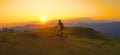 AERIAL: Mountain biker riding his bicycle up a grassy hill at picturesque sunset Royalty Free Stock Photo