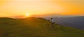 AERIAL: Mountain biker riding his bicycle up a grassy hill at picturesque sunset Royalty Free Stock Photo