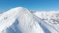 AERIAL: Unrecognizable skier hiking up the snowy mountain in sunny winter.