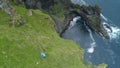 AERIAL Unrecognizable tourist hiking in Faroe Islands taking photos from a cliff