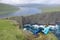 AERIAL: Unrecognizable woman sits on the edge of a cliff and looks at the lake.
