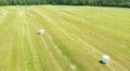 Aerial view agricultural landscape. Straw packages on field. Flying over cereal bale of hay wrapped in plastic white foil.