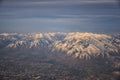 Aerial view from airplane of the Wasatch Front Rocky Mountain Range with snow capped peaks in winter including urban cities of Pro