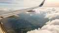 Airplane wing soaring above fluffy white clouds with green patchwork fields and winding river below Royalty Free Stock Photo