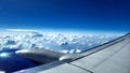 Aerial view of an airplane wing hovering above the clouds in a clear blue sky Royalty Free Stock Photo