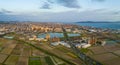 Aerial view as wide road curves through plowed fields to small coastal town