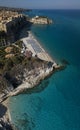 Aerial view of a beach with umbrellas and bathers. Houses on the rock and beach. Promontory. Tropea, Calabria, Italy.