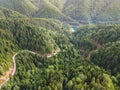 Aerial view of a beautiful curvy road by the lake and the green woods of high mountains Royalty Free Stock Photo