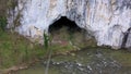 Aerial view of a big cave entrance and mountain river by drone, Unguru Mare cave, Suncuius, Romania