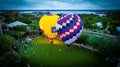 Aerial view of brightly-colored hot air balloons in a park preparing to take off