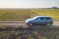 Aerial view of car driving by straight ground road through green fields on sunny blue sky copy space background. Drone photography