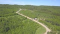 Aerial view of car moving on the countryside road near the cottages surrounded by meadows and forest with coniferous and Royalty Free Stock Photo