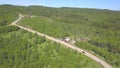 Aerial view of car moving on the countryside road near the cottages surrounded by meadows and forest with coniferous and Royalty Free Stock Photo