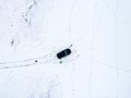 Aerial view of a car parked on a snowy field covered in footprints in winter