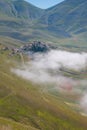 Aerial view of Castelluccio di Norcia mountain village with fog at early morning on summer day, Umbria, Italy