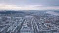 Aerial view of city buildings covered with snow, roads and large river on the background against grey evening sky in Royalty Free Stock Photo