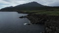 Aerial view of cliff, mountain and sea shore. Clip. Forested slipping volcano against the cloudy sky.