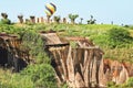 Aerial view of colorful hot-air-ballon above lush green vegetation of steep rocky hill