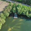 Aerial view of the corner of a pond with a small wooden fishing hut and a landing stage, trees at the bank