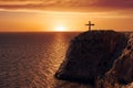 Aerial view of a crucify on the edge of a cliff against the sea and sunset.