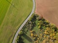 Aerial view of a curvy road between trees, plowed farmland and grassland on a warm and sunny day in autumn Royalty Free Stock Photo