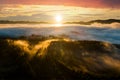 Aerial view of dark green pine trees in spruce forest with sunrise rays shining through branches in foggy fall mountains Royalty Free Stock Photo