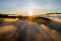 Aerial view of dark green pine trees in spruce forest with sunrise rays shining through branches in foggy fall mountains Royalty Free Stock Photo