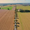 Aerial view of a dead straight narrow asphalted country road with trees at the edge between fields and meadows in Germany