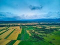 Aerial view from drone flight over different agricultural fields and mountains behind with clouds