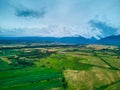 Aerial view from drone flight over different agricultural fields and mountains behind with clouds