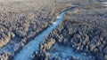 Aerial view from a drone of a road in the middle of snow-covered trees and snow-covered forest on a winter day. A dense