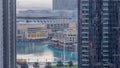 Aerial view of Dubai Fountain in downtown with palms in park next to shopping mall and souq night to day timelapse, UAE