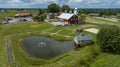 Aerial View Of A Farm Complex With Red Barns, A Large Pond With A Fountain, A Stone House