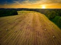 An aerial view of a field of freshly baled hay with a rising sun in the background.