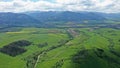 Aerial view of fields, meadows and hills under High Tatras mountains, some settlements and roads also visible.