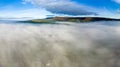 Aerial view flying over a bank of fog over a large large surrounded by mountains (Llangorse Lake, Wales