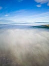 Aerial view flying over a bank of fog over a large large surrounded by mountains (Llangorse Lake, Wales