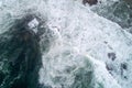 aerial view of the foamy waves breaking against the rocks of the shore