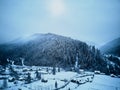 Aerial view of foggy countryside and houses in snowy valley. Hills and mountains with pine tree forest covered in snow Royalty Free Stock Photo