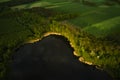 Aerial view of a forest lake. shoreline of a wild lake, surrounded by green trees, seen from a drone. Fields in the background