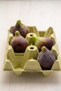 Aerial view of four figs in yellow egg carton, on white wooden table,