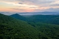 Aerial view of green pine forest with dark spruce trees covering mountain hills at sunset. Nothern woodland scenery from