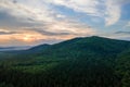 Aerial view of green pine forest with dark spruce trees covering mountain hills at sunset. Nothern woodland scenery from