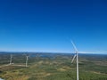 Aerial view of green valleys and hills with tall wind turbines under the clear blue sky