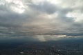 Aerial view from high altitude of distant city covered with puffy cumulus clouds forming before rainstorm in evening