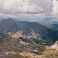 Aerial view of a High mountain valley with a small blue lake down the mountain clouds in the sky and sun spots on the cliffs Royalty Free Stock Photo