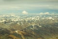 A aerial view of Himalayan desert mountains with snowy peaks under white clouds and blue sky Royalty Free Stock Photo