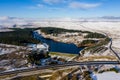 Aerial view of a large reservoir next to a major dual carriageway on a snowy day