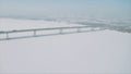 Aerial view of a long bridge above snow and ice covered river between two parts of a city. Clip. Winter landscape with a